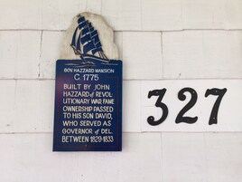 Ein historisches Schild an einer weißen Wand mit der Nummer 327.