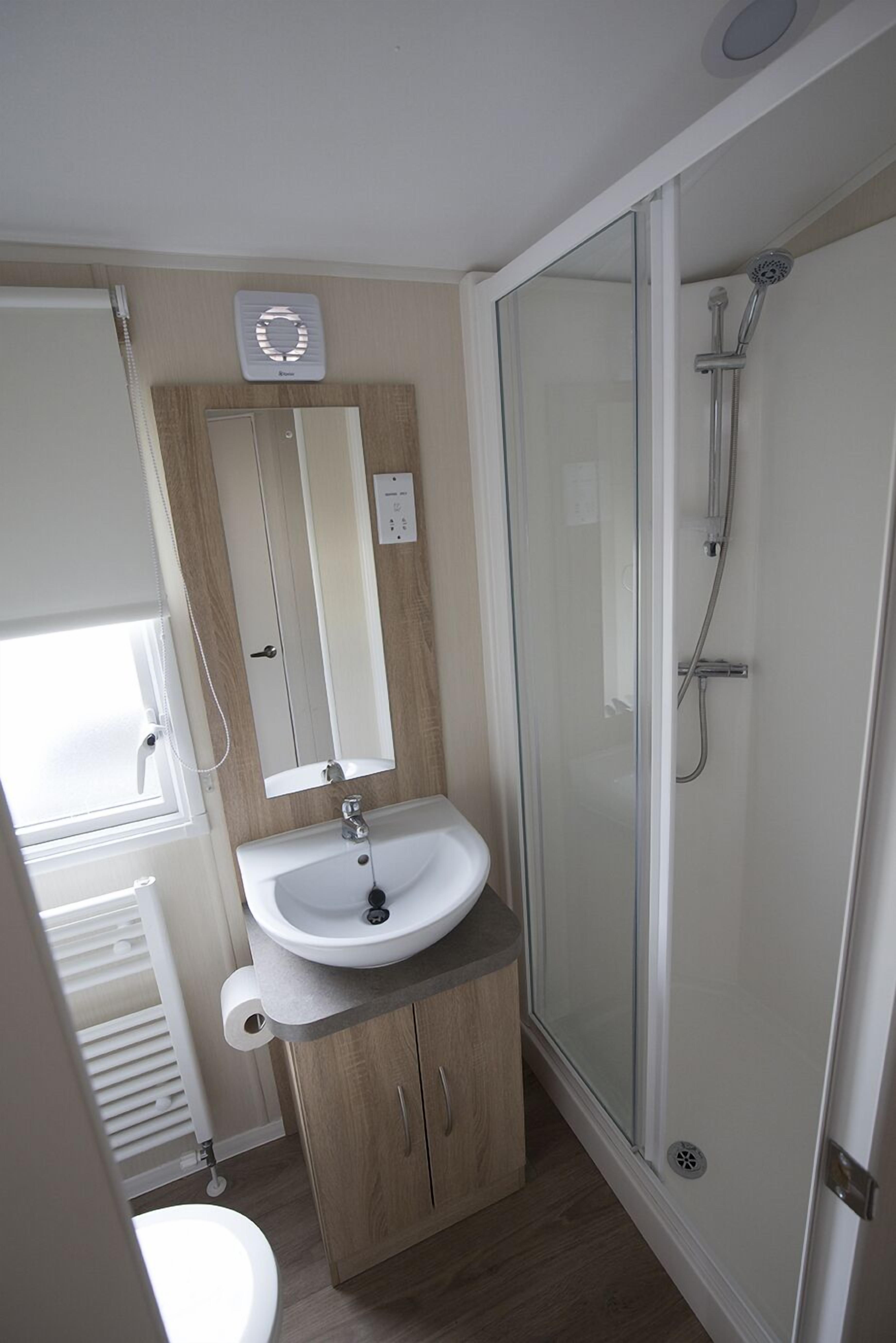 A bathroom with a glass-enclosed shower, a sink with a mirror above it, and a toilet.