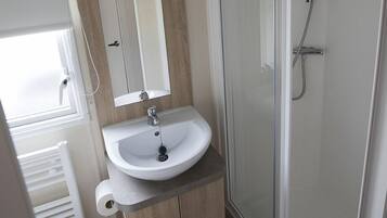 A bathroom with a glass-enclosed shower, a sink with a mirror above it, and a toilet.