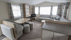 A modern RV interior with a sofa, dining table, TV, and storage cabinets. - Waterside Holiday Park & Spa (Weymouth)