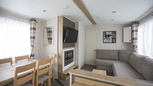 A compact living space with a dining area, a sofa, a fireplace, and a television. - Waterside Holiday Park & Spa (Weymouth)
