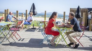 A wooden deck with colorful chairs and tables, overlooking a beach. - Waterside Holiday Park & Spa (Weymouth)