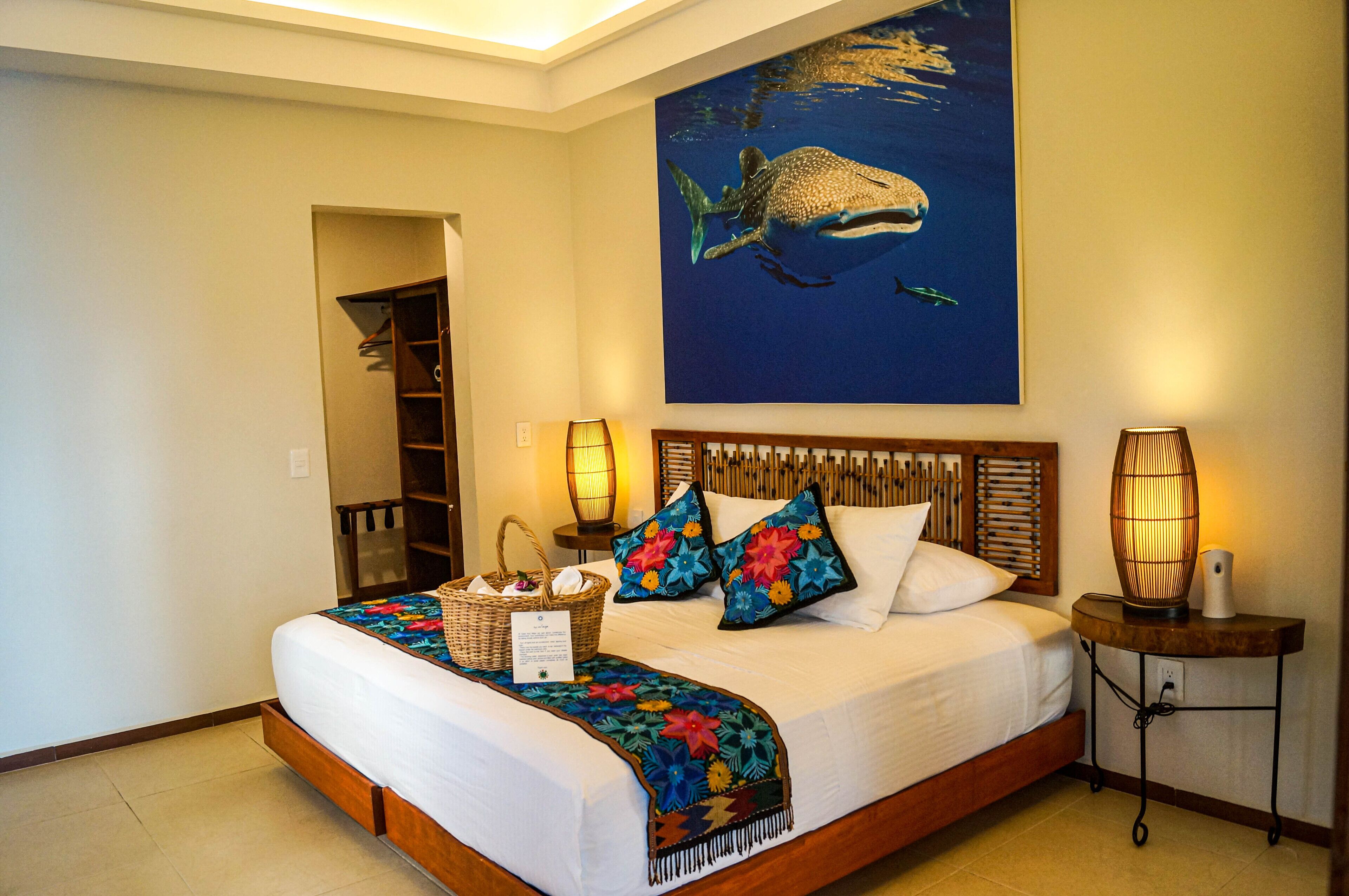 Habitación de hotel con una cama, un cuadro grande de una ballena en la pared, dos lámparas de noche y un cabecero de madera.
