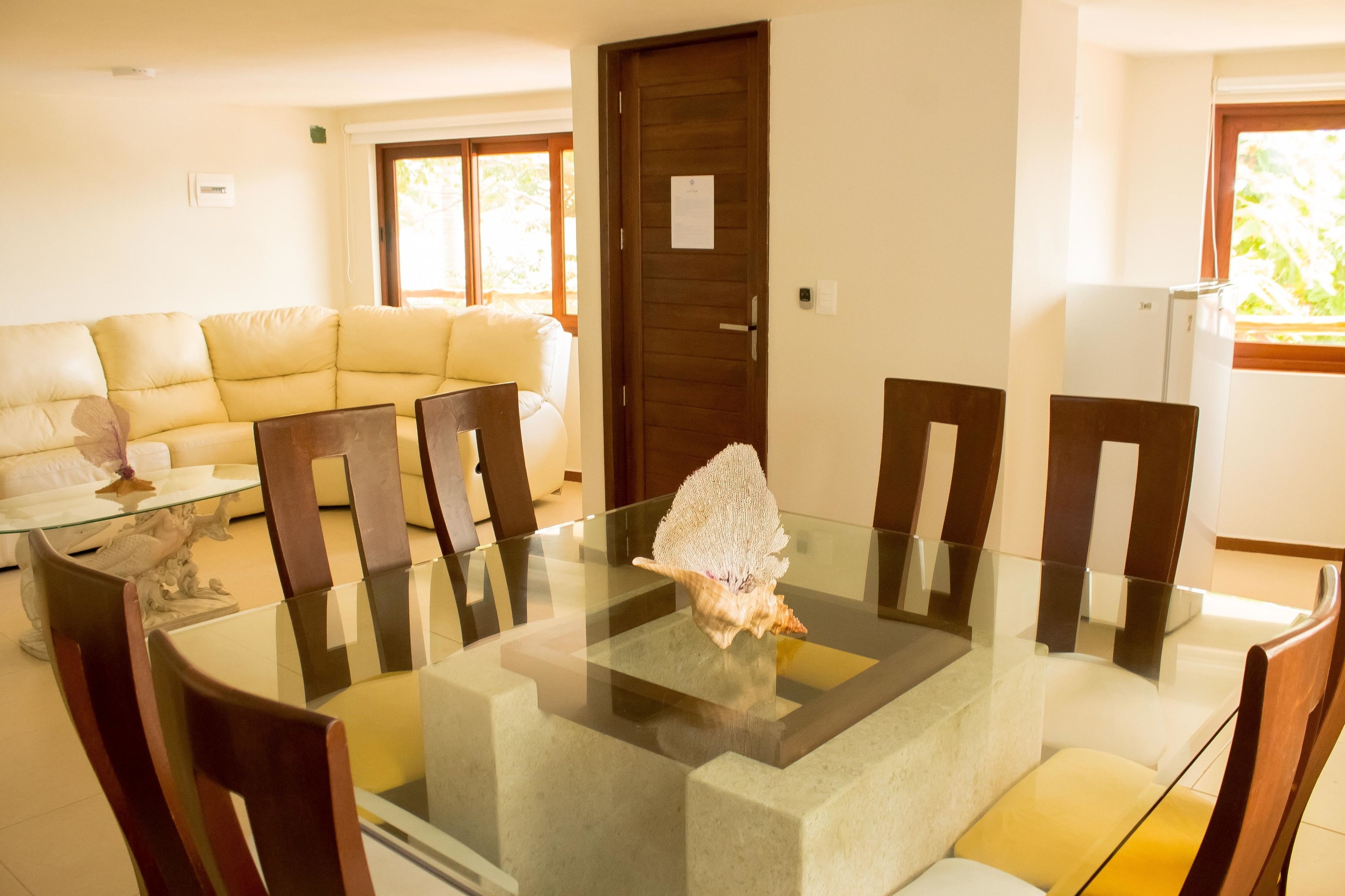 A dining area with a glass-top table, wooden chairs, and a decorative shell centerpiece.