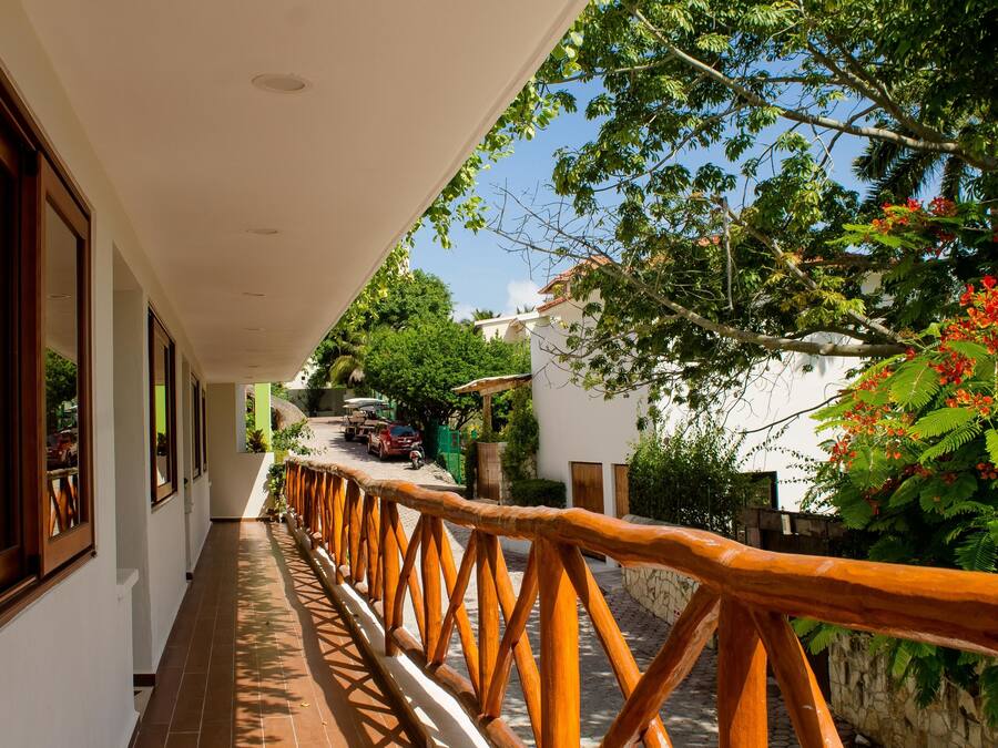 A corridor with a wooden railing, white walls, and a view of a street with parked cars and greenery.