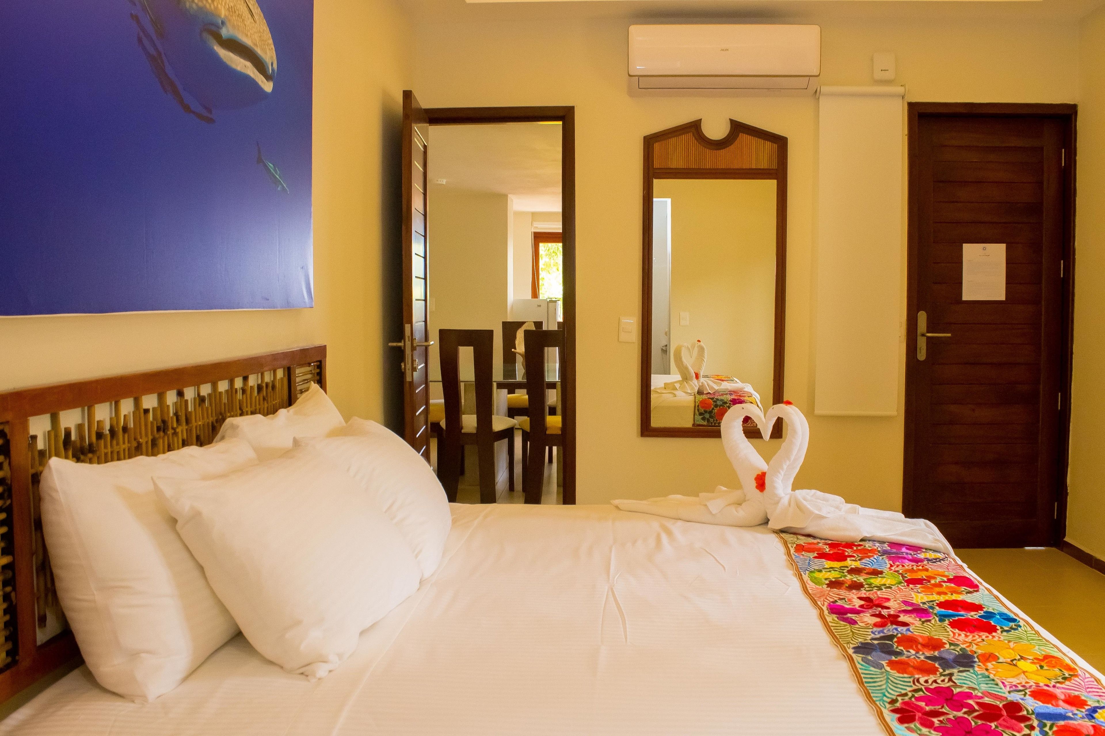 Una habitación de hotel con cama, espejo, puerta y un cuadro en la pared.