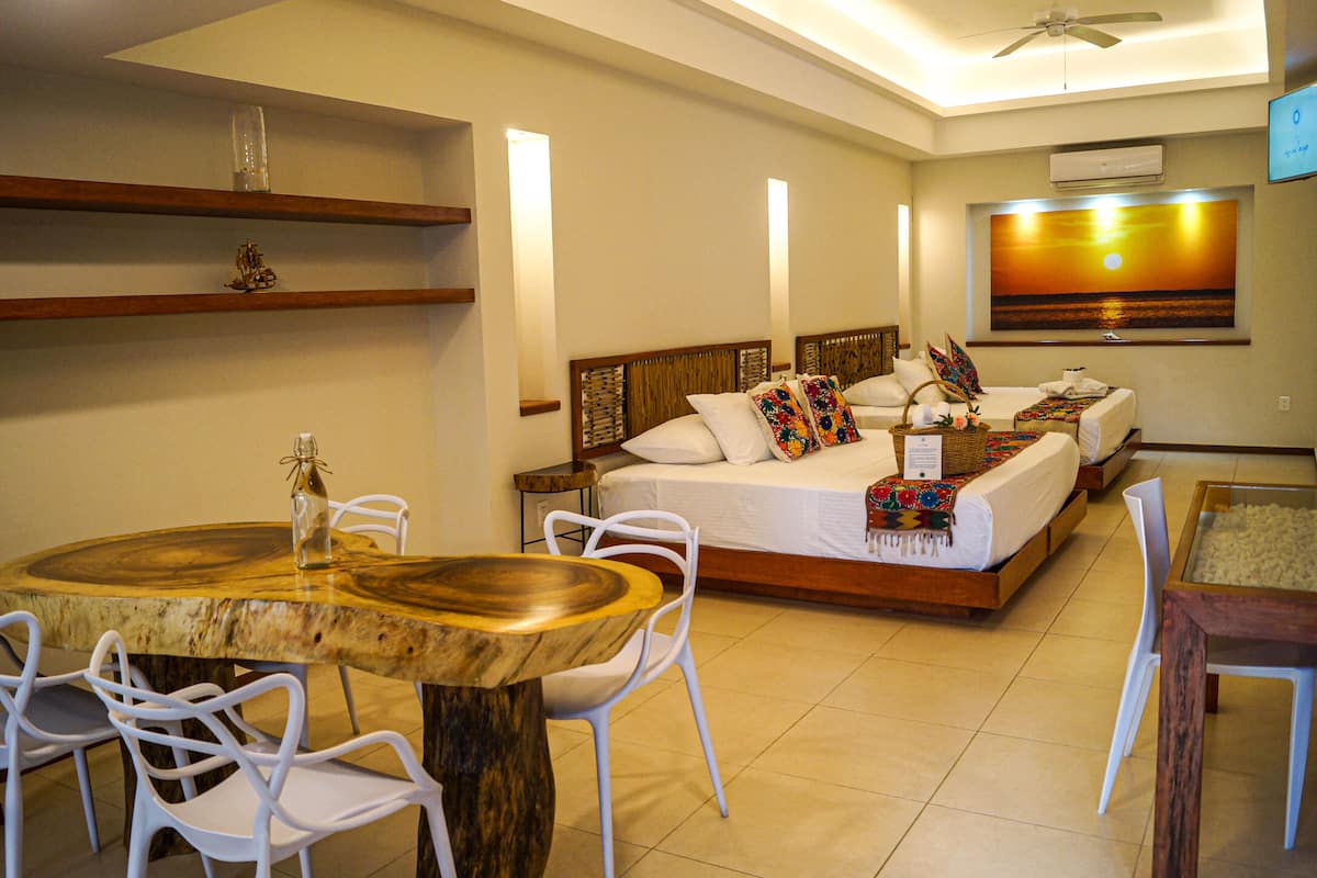 Una habitación de hotel con una cama de madera, sillas blancas, una mesa de comedor de madera y un cuadro en la pared.
