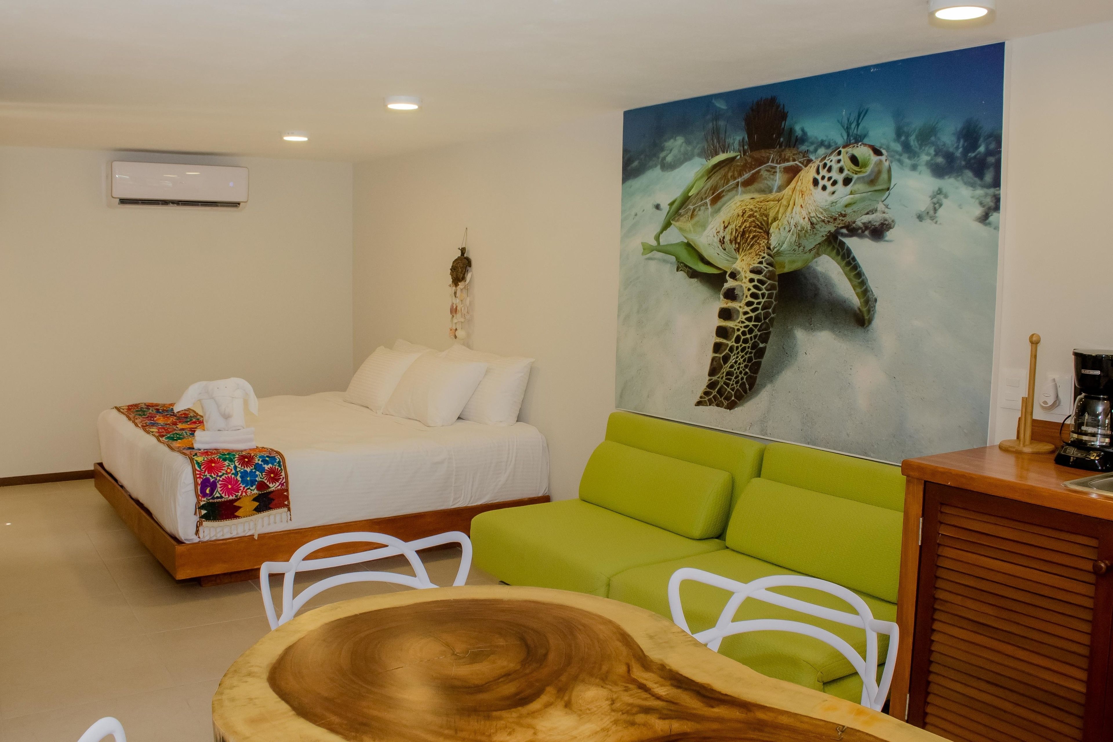 Une chambre d’hôtel avec un lit, un canapé vert, une table en bois et un tableau représentant une tortue de mer.