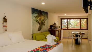 Una habitación de hotel con cama, un sofá verde, una mesa de comedor con sillas y un cuadro grande de una tortuga marina en la pared.
