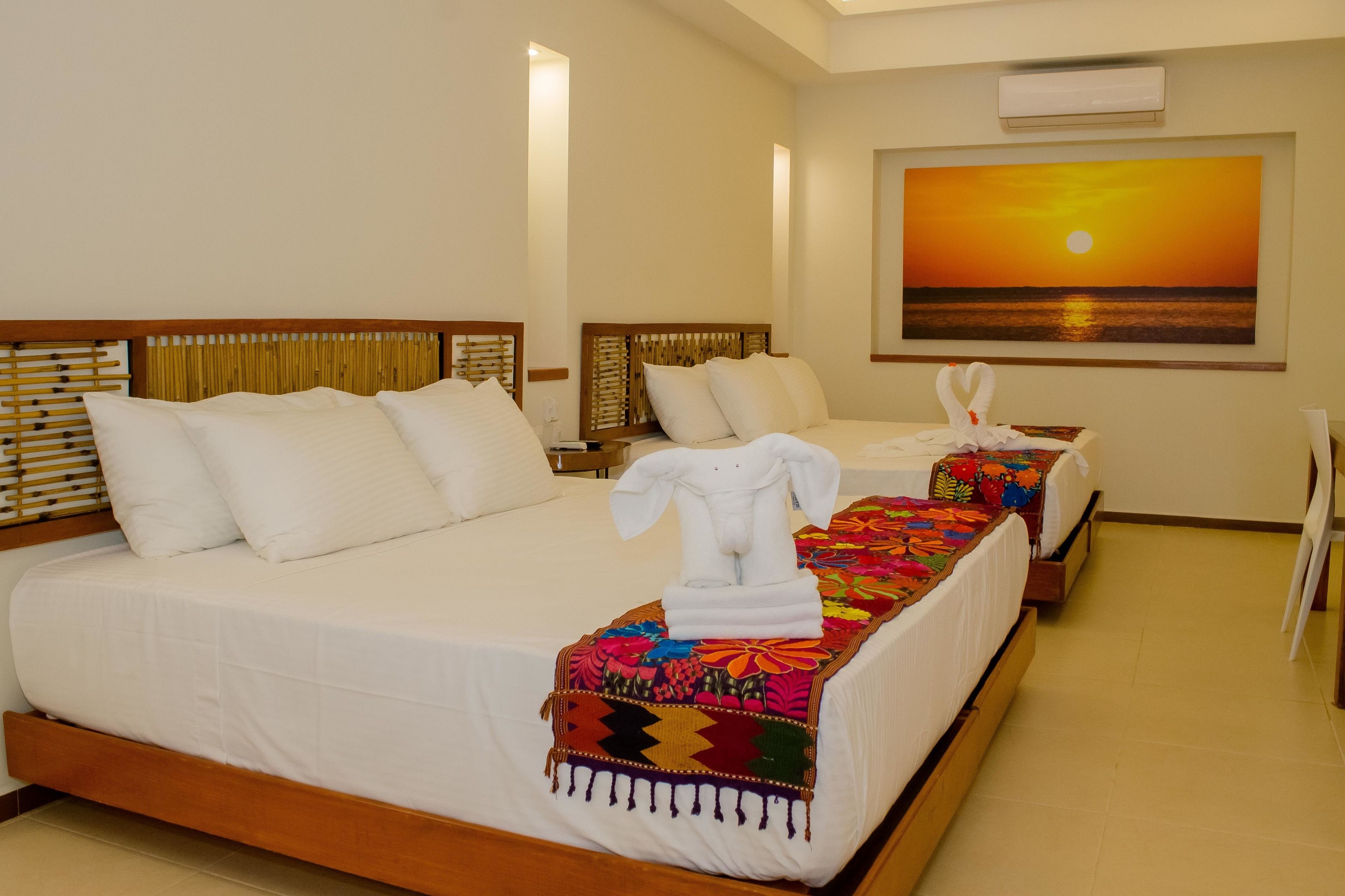 Quarto de hotel com duas camas, uma grande pintura de um pôr do sol e um porta-toalhas com toalhas.
