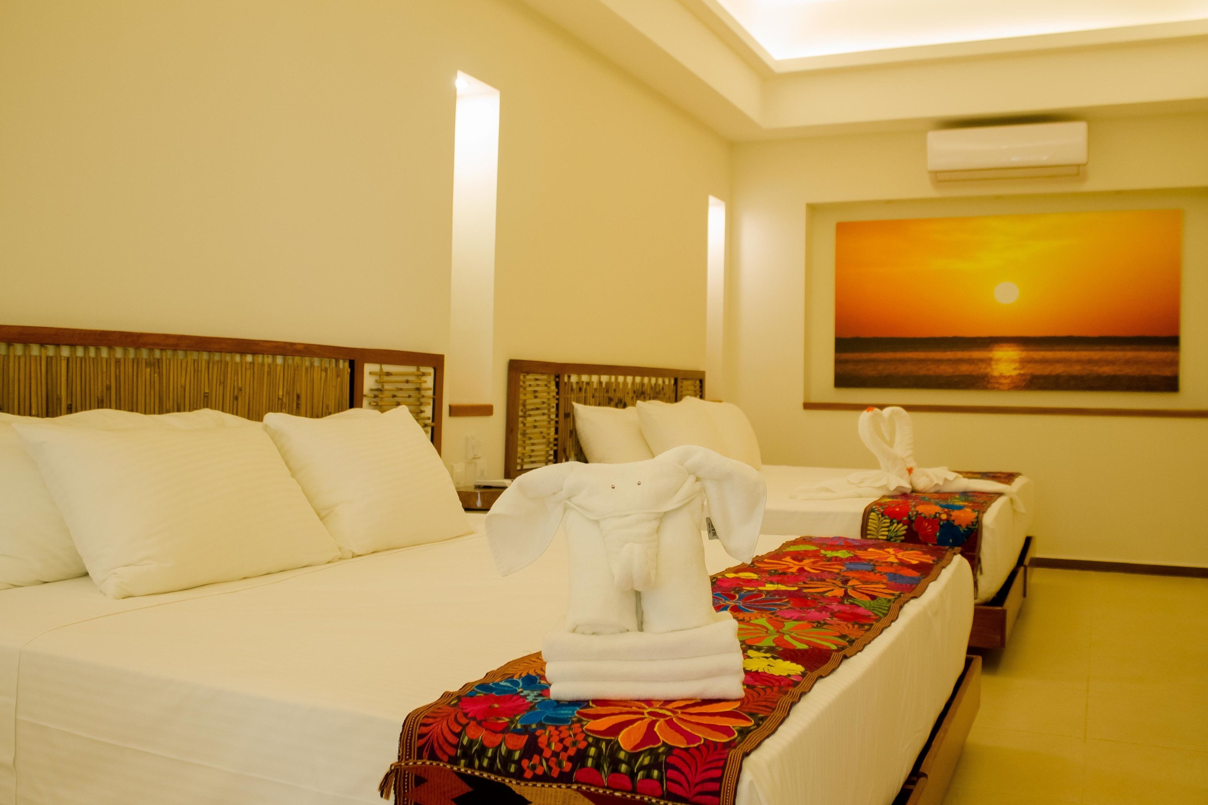 A hotel room with two beds, a colorful floral bedspread, white linens, and a painting of a sunset on the wall.