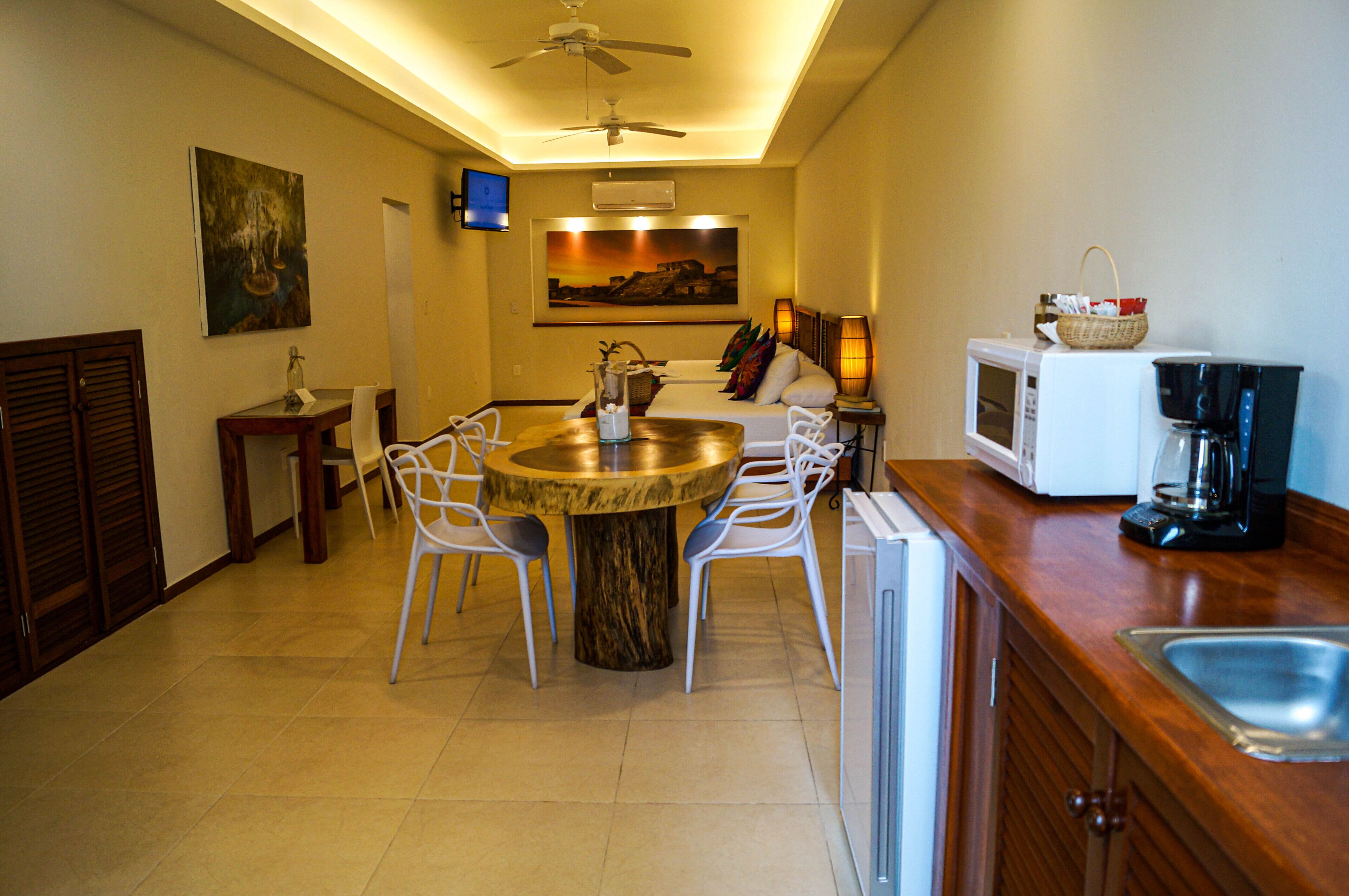 Une cuisine moderne avec une table de salle à manger ronde, des chaises blanches, un ventilateur de plafond, un téléviseur et une machine à café.