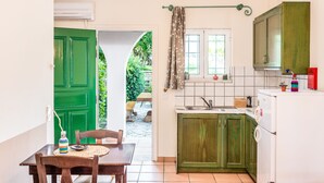 Een compacte keuken met groene kastjes, een witte koelkast en een eethoek met een houten tafel en stoelen.