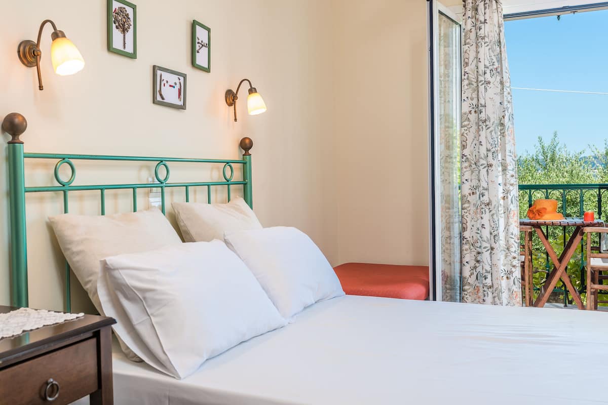 A bedroom with a green metal headboard, white bedding, and a balcony with a table and chairs.