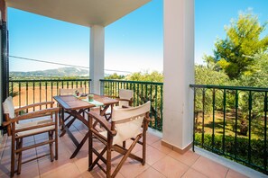 Ein Balkon mit Tisch und Stühlen, der einen Blick auf einen Garten und ferne Hügel bietet.