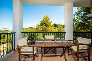 A wooden table and chairs on a balcony with a view of trees and a clear sky.