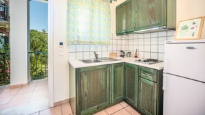 Een keuken met groene kastjes, een wit aanrechtblad en een raam met een gordijn met dessin.
