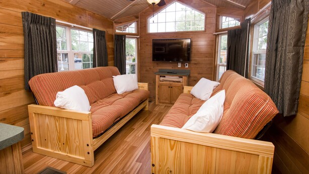 Een houten blokhut interieur met twee banken, een plafondventilator en een flatscreen-televisie.