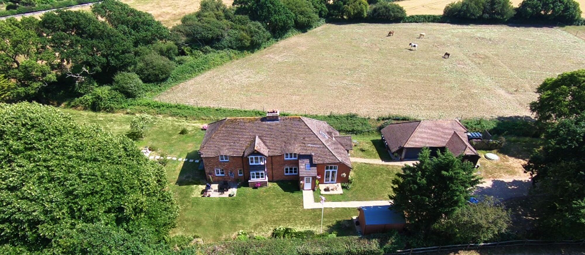 A two-story house with a large front yard and a fenced field in the background.