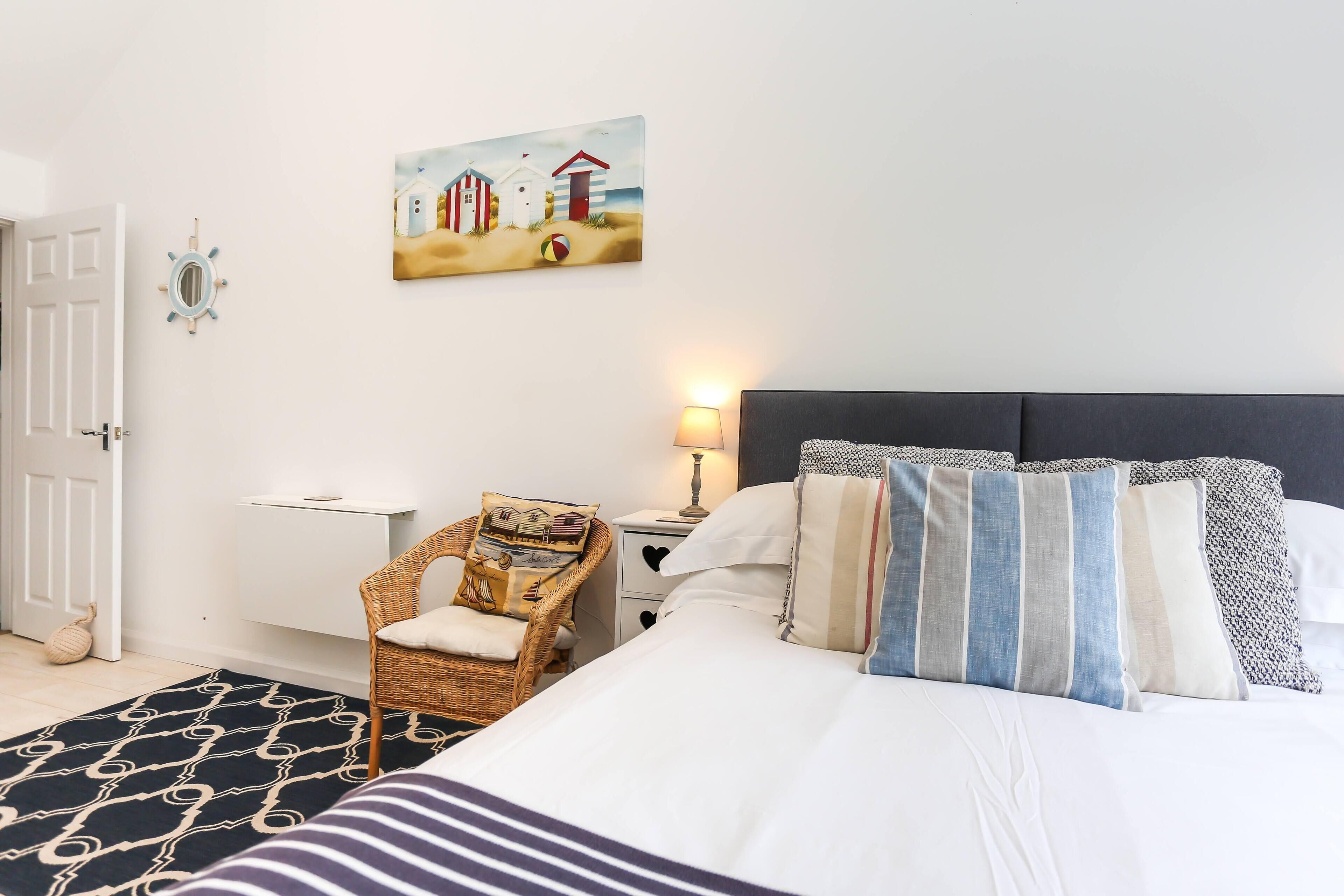 A bedroom with a bed, a chair, a nightstand, a lamp, and a painting on the wall.