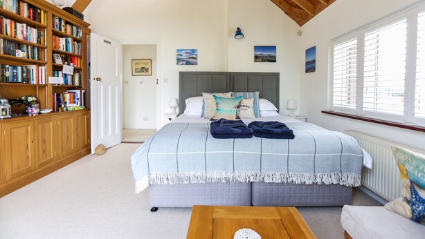 Quarto com cama grande, estante e janela com persianas.