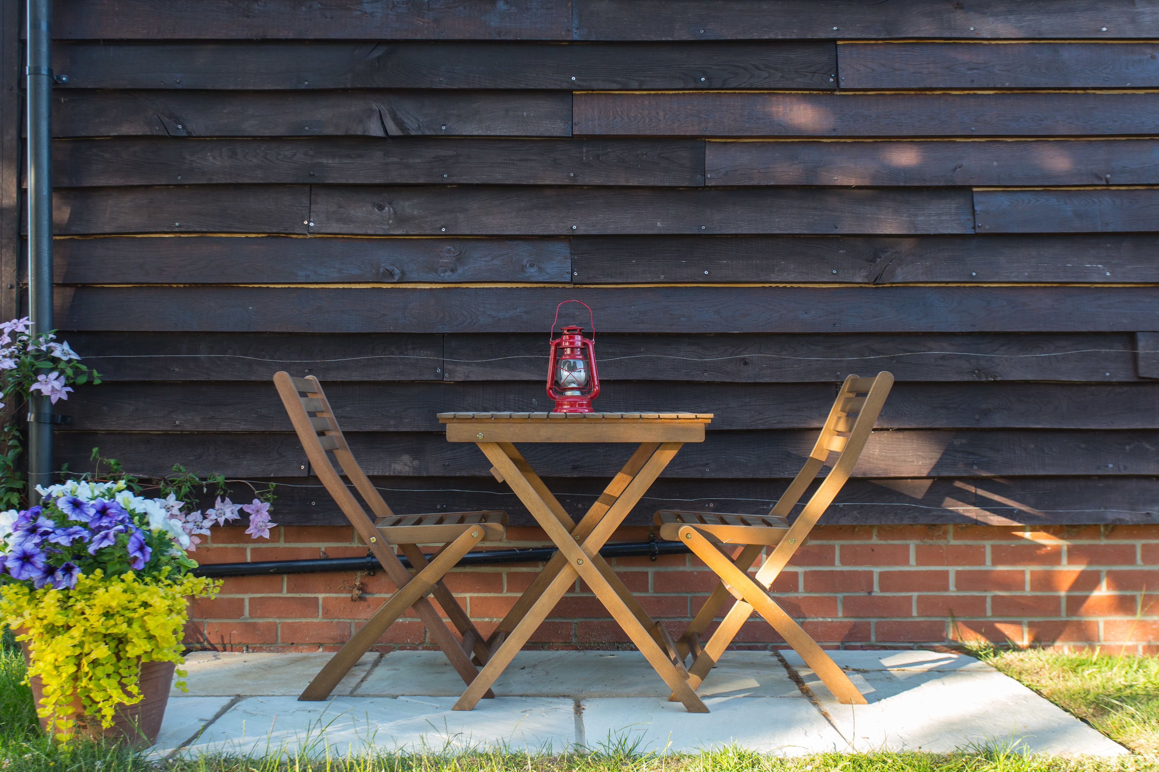 Une table et des chaises en bois, placées devant un mur de briques et séparées par une clôture en bois.