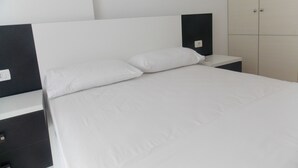 A neatly made bed with white bedding and two pillows, a bedside table with a lamp, and a wardrobe with a handle. - Belvedere Apartaments 2 (Sarandë)
