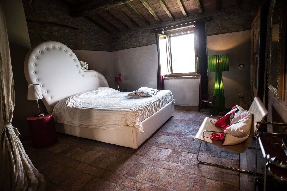 A bedroom with a large bed, a small table, a chair, a lamp, and a window.