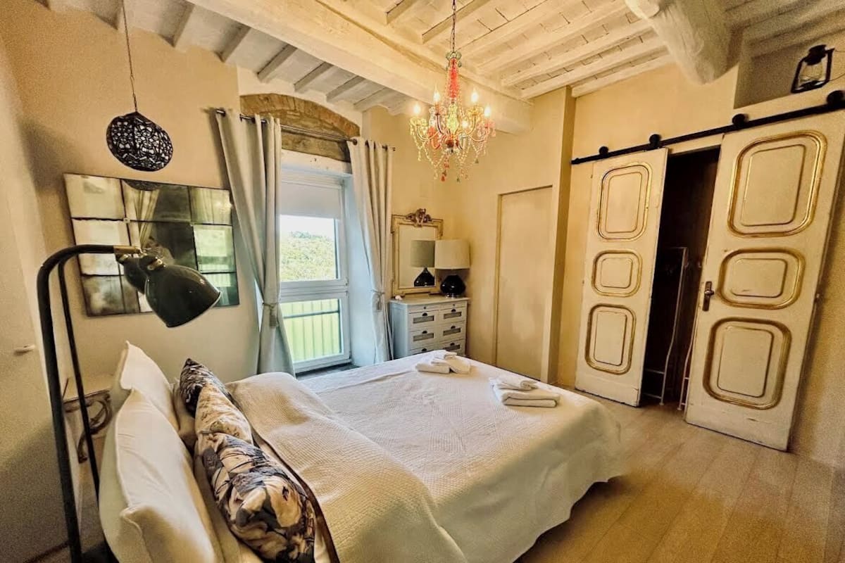A bedroom with a bed, a desk, a chair, a chandelier, and a wardrobe.