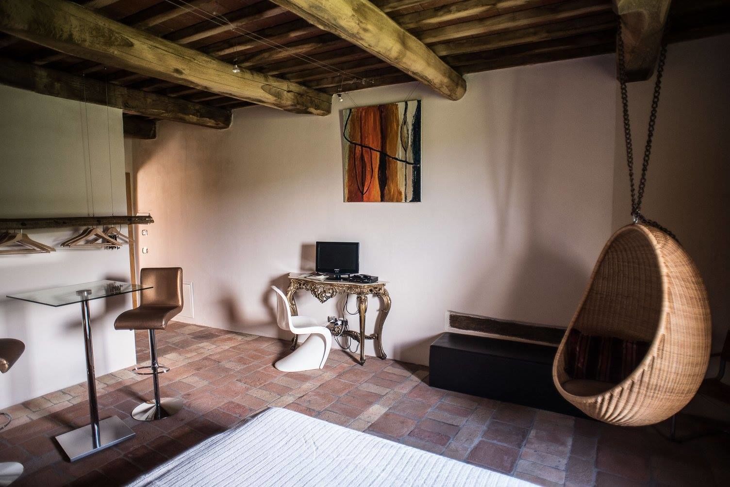 Una stanza con una poltrona sospesa, un tavolo con un computer e un quadro appeso al muro.