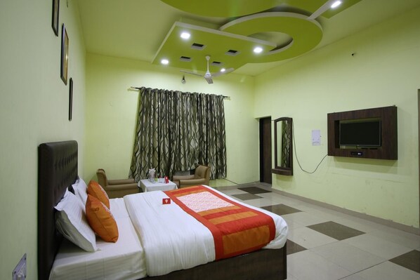 A hotel room with a bed, a TV, a ceiling fan, and a window with curtains. - Motel Divine International (Roorkee)