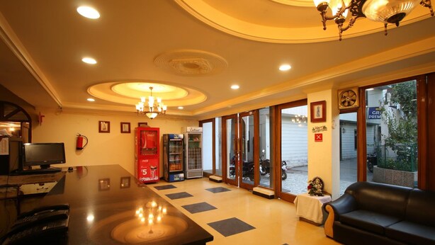 A lobby with a reception desk, a red vending machine, a sofa, and a large window with a view of the street. - Motel Divine International (Roorkee)