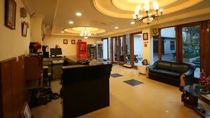 A hotel lobby with a reception desk, a black leather sofa, and a chandelier. - Motel Divine International (Roorkee)