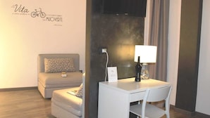 Una habitación de hotel moderna con sofá, una mesita con lámpara y televisor montado.