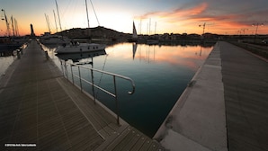 Un puerto deportivo con barcos amarrados, un muelle de madera y una masa de agua tranquila que refleja el atardecer.