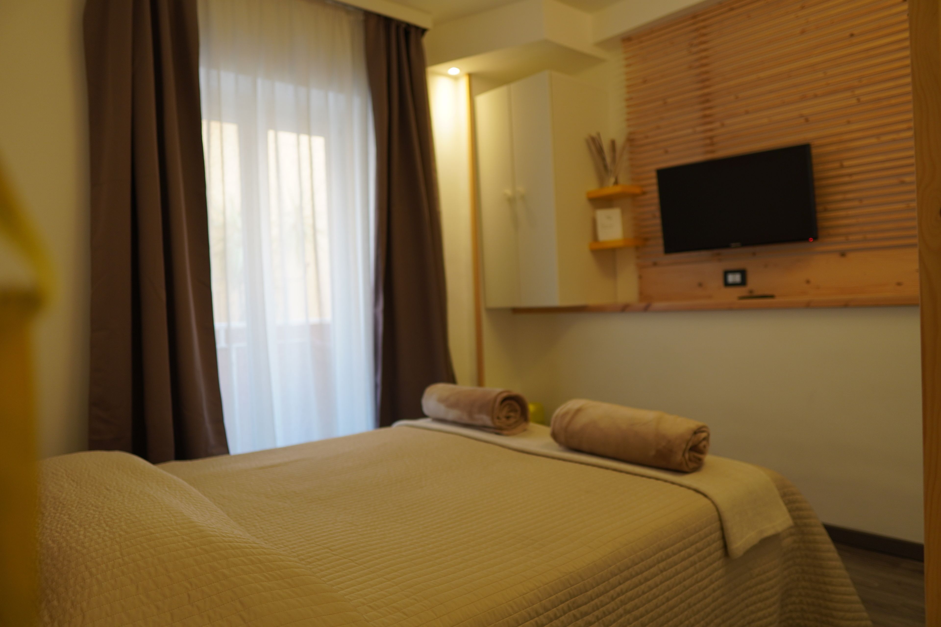 Una habitación de hotel con cama, televisión en la pared y ventana con cortinas.