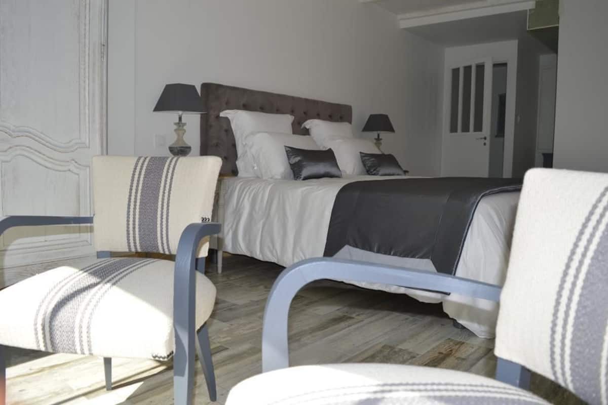 A bedroom with a bed, two bedside tables with lamps, a chair, and a door.