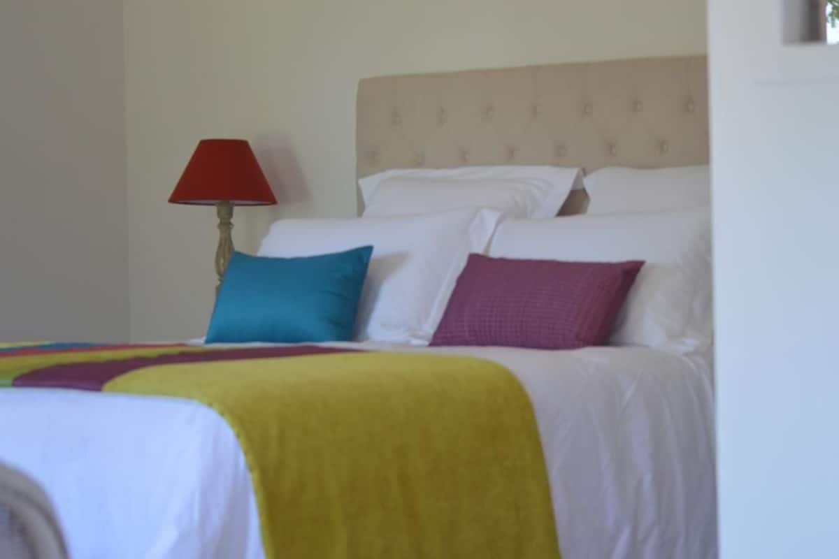 A hotel room with a bed, a red lamp, and a yellow blanket.