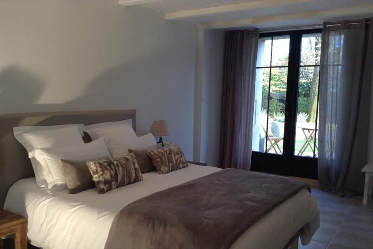 A bedroom with a large bed, a nightstand, and a window with curtains.