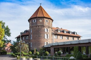 Un edificio histórico con una torre destacada, un patio con setos cuidados y un anexo moderno con grandes ventanales.