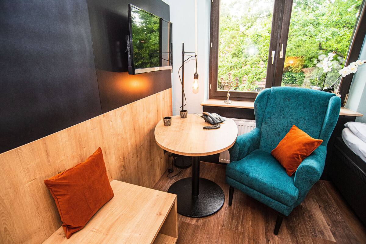 A cozy room with a wooden bench, teal armchair, and a small round table with a phone and lamp.