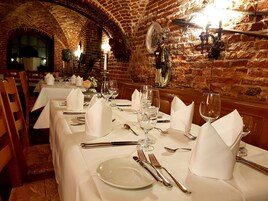 Un restaurante con paredes de ladrillo y techos abovedados, mesas dispuestas con manteles blancos, cubertería y copas de vino.