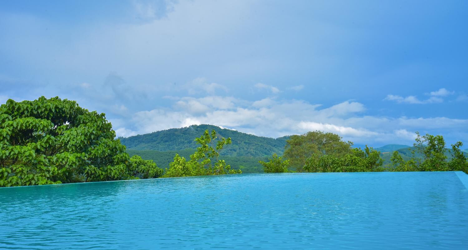 A clear blue pool with a view of lush green hills and a partly cloudy sky.