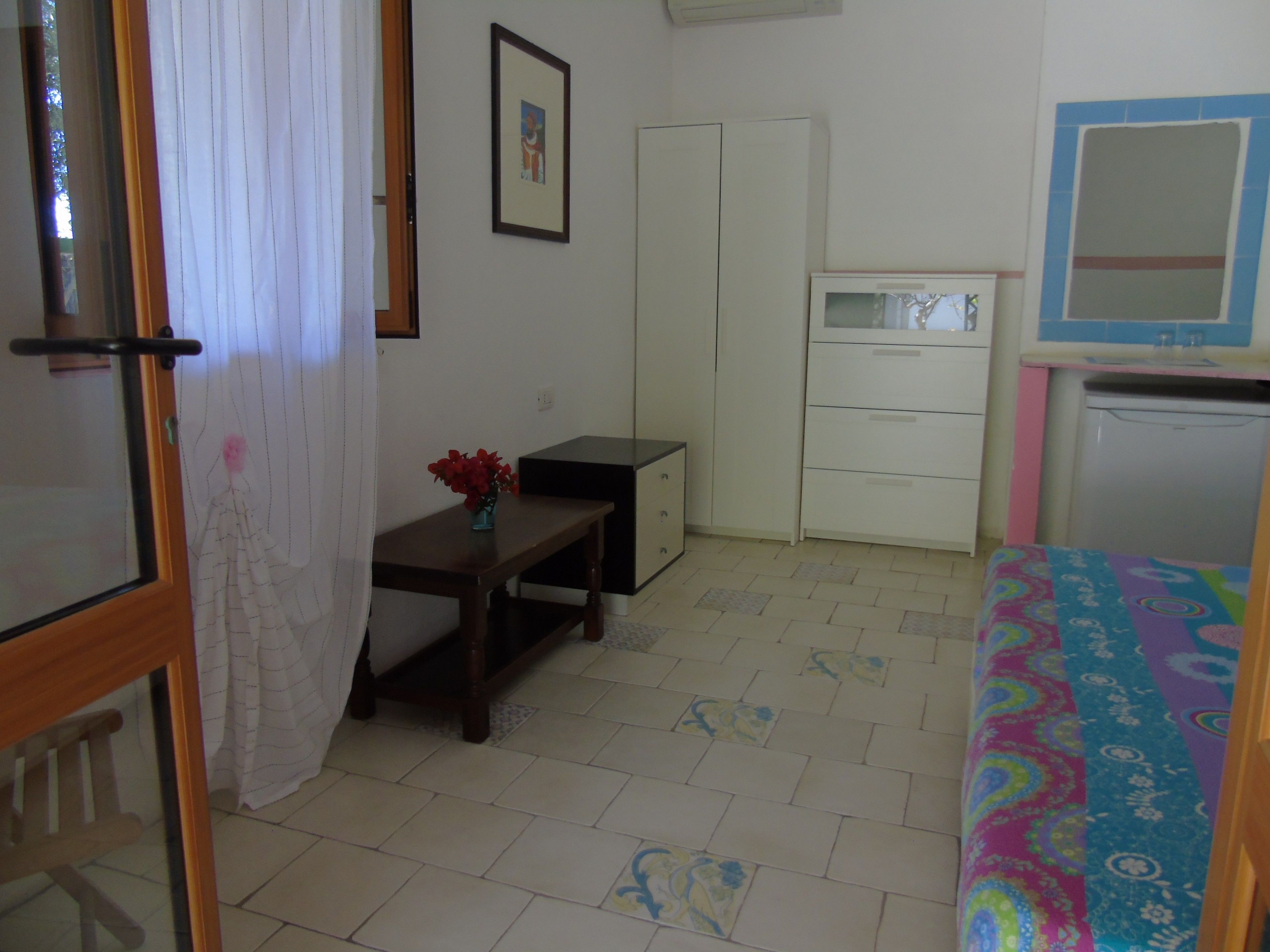 A bedroom with a bed, a desk, a chair, a wardrobe, and a small kitchenette.