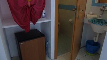 A bathroom with a shower, toilet, sink, and a small refrigerator.