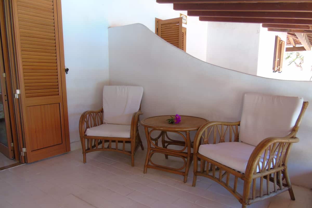 A corner of a room with two wicker chairs and a small round table, a wooden door, and a white wall.