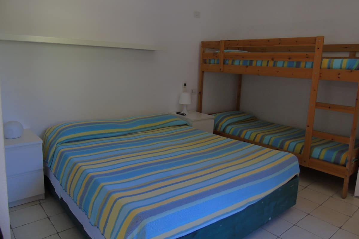 A room with two bunk beds, a bedside table with a lamp, and a striped bedspread.