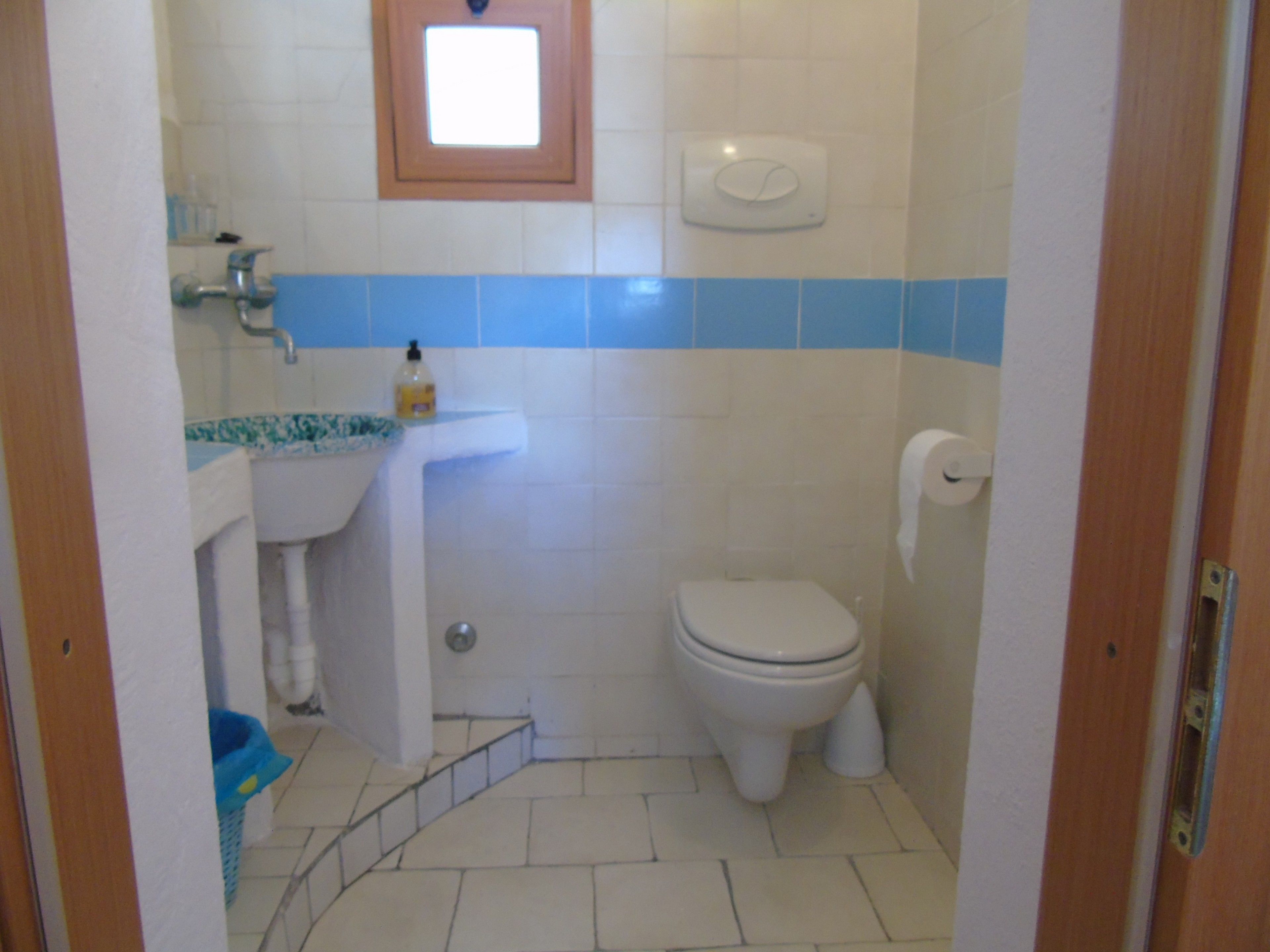 Een kleine badkamer met toilet, wastafel en een raam.