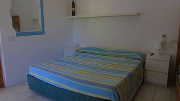 Un dormitorio con cama, mesita de noche, espejo y estante con un florero.