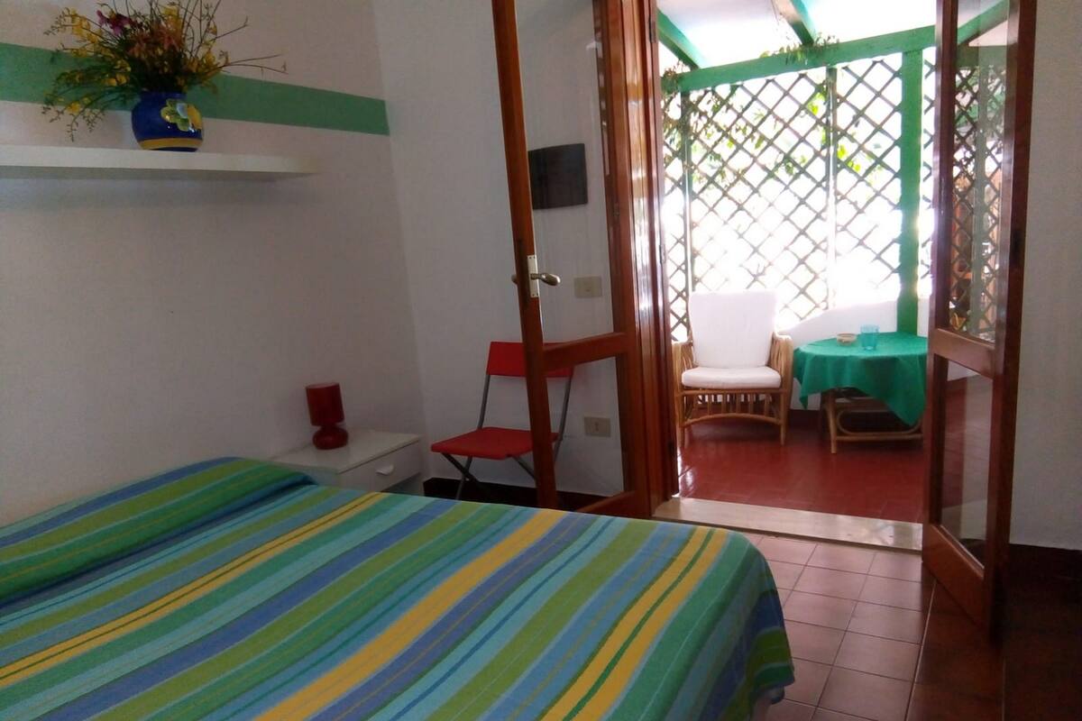 A room with a bed, a chair, a table, and a view through a door.